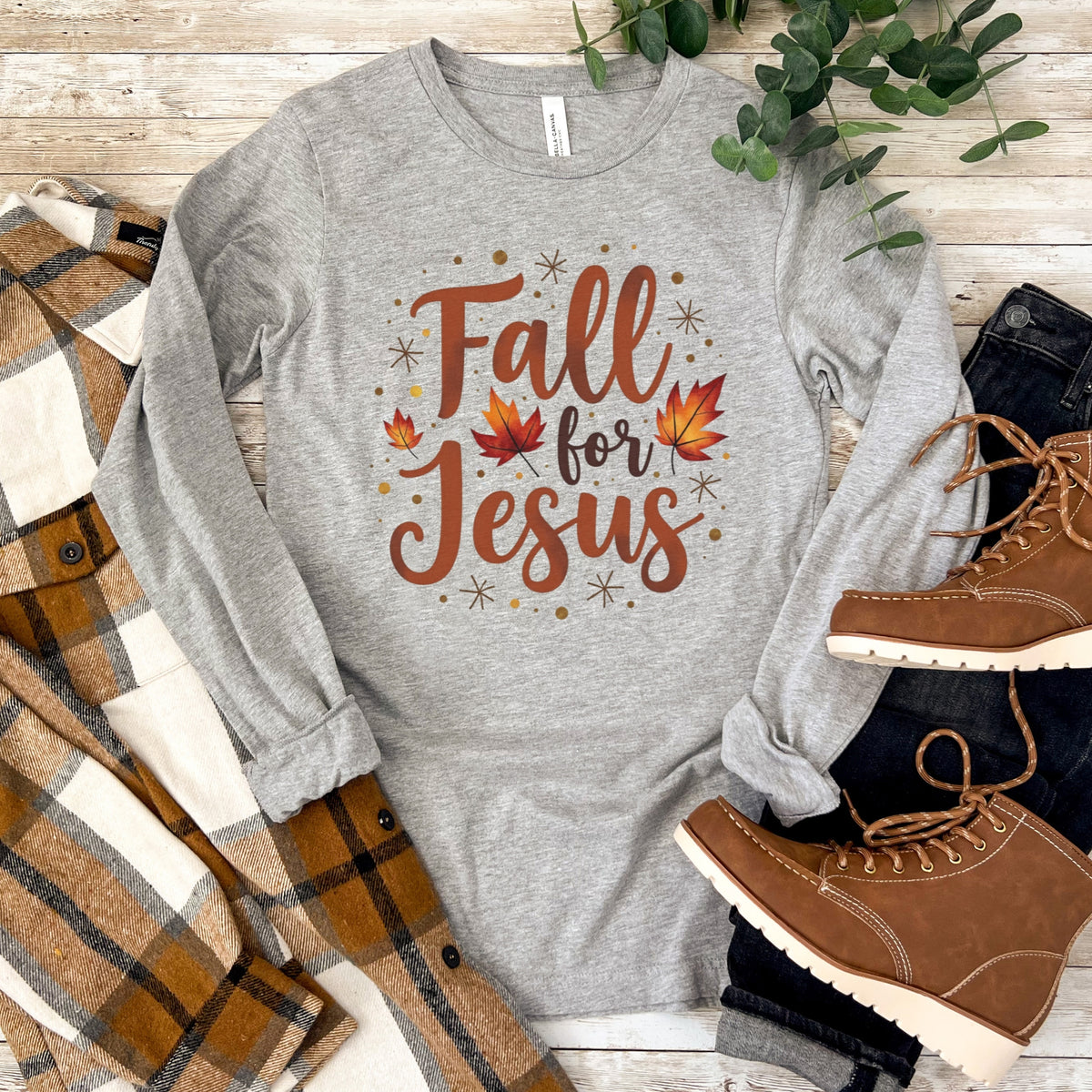 Gray long sleeve tee with 'Fall for Jesus' text, plaid blanket, and brown boots on a wooden surface.