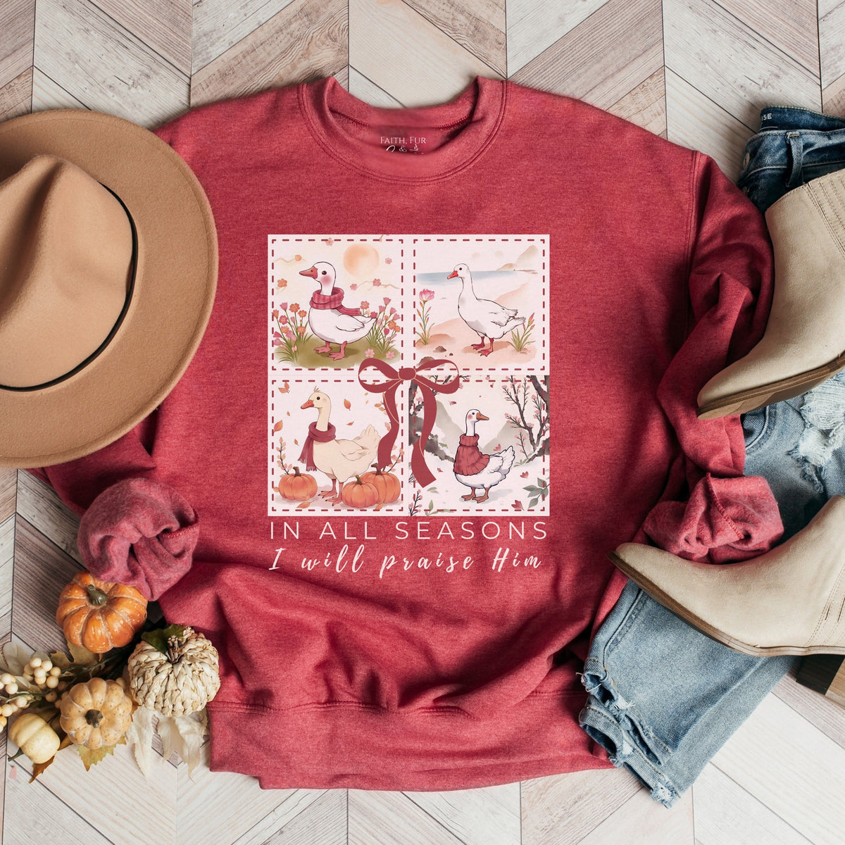 Red sweatshirt with a graphic design and text, surrounded by autumn-themed items on a wooden floor.