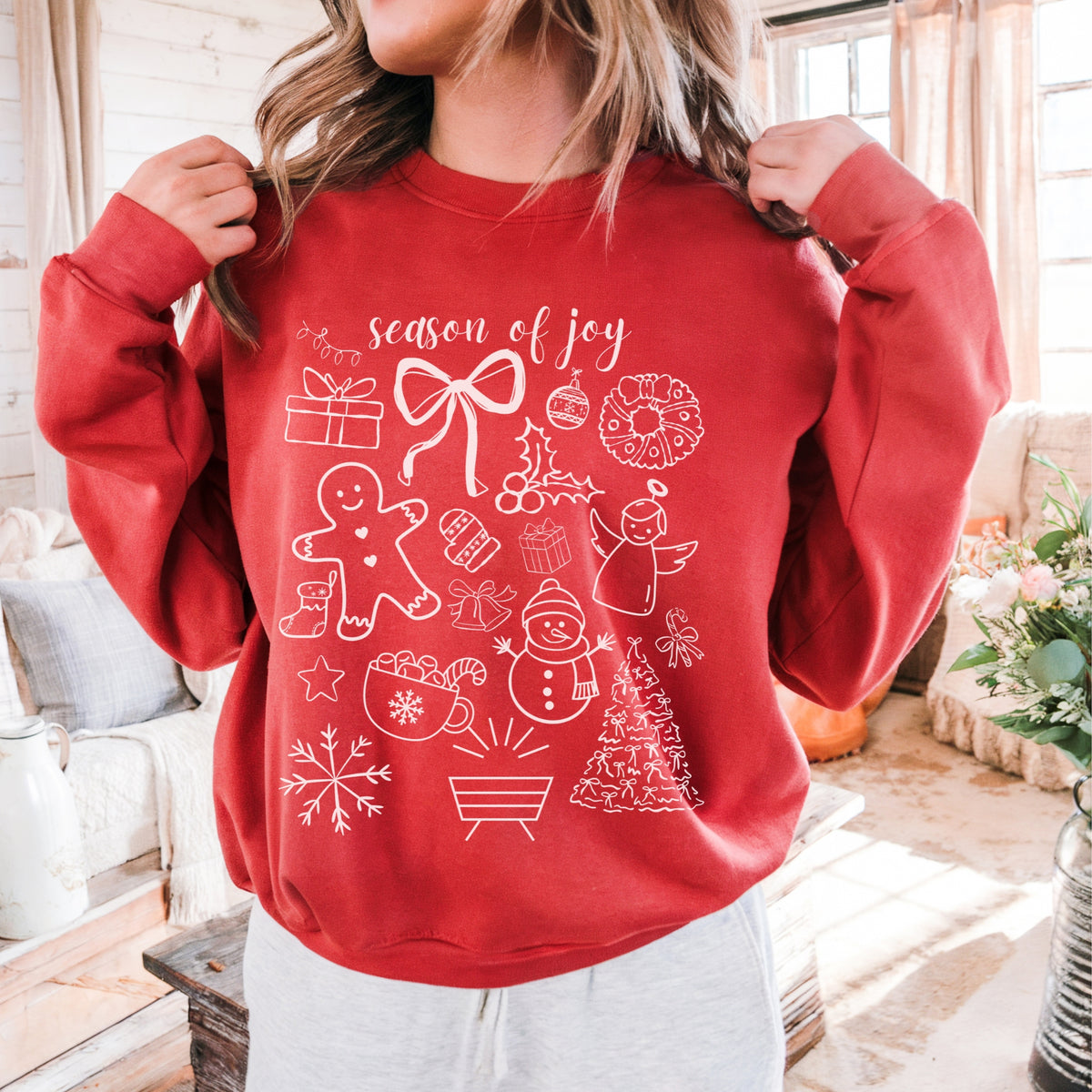Red sweatshirt with Christmas-themed designs and text 'season of joy' worn by a person in a home setting.