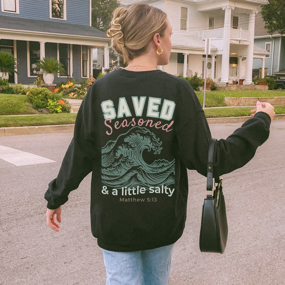 Person wearing a black sweatshirt with text and graphics, walking on a street.