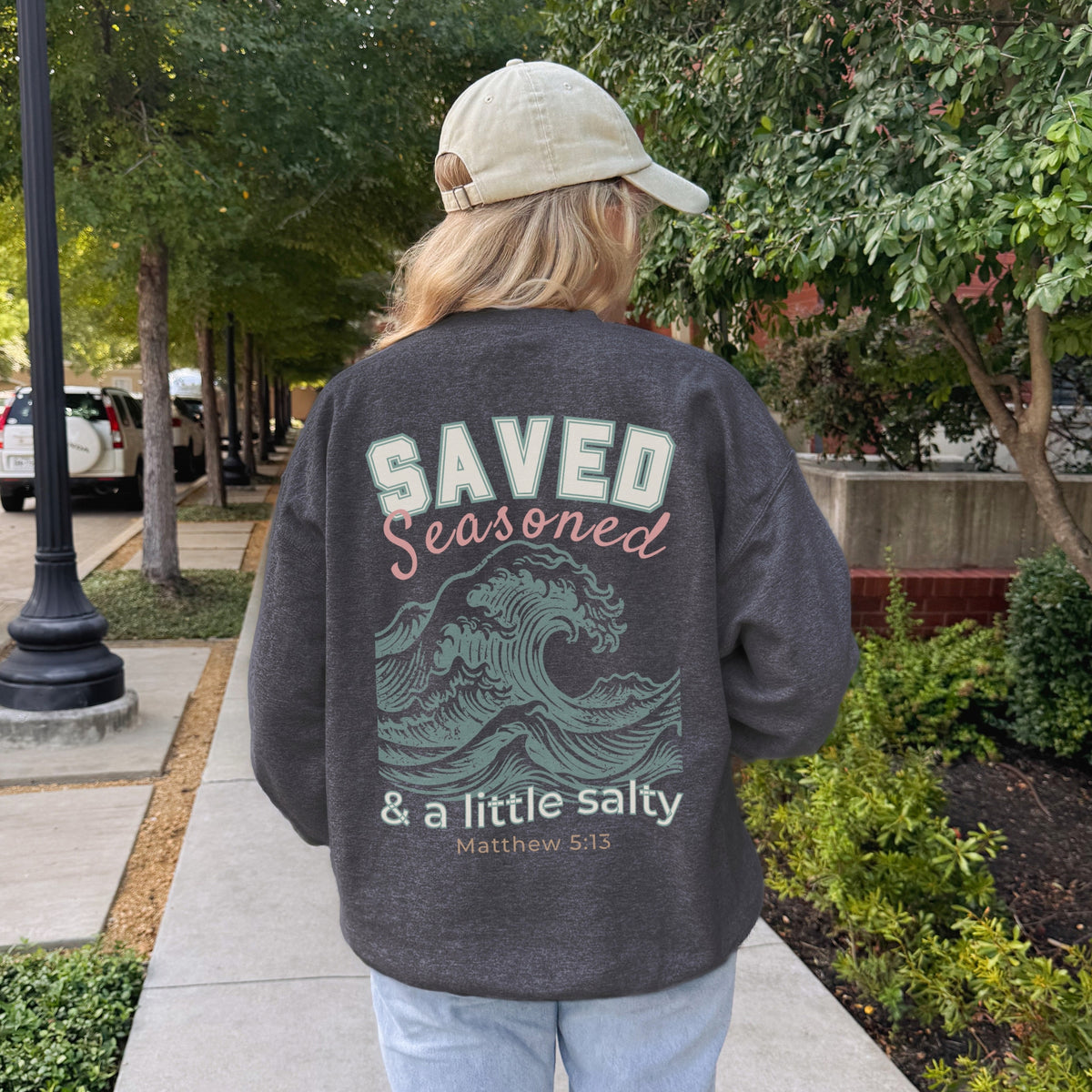 Person wearing a dark gray sweatshirt with text and graphics on the back, walking outdoors.