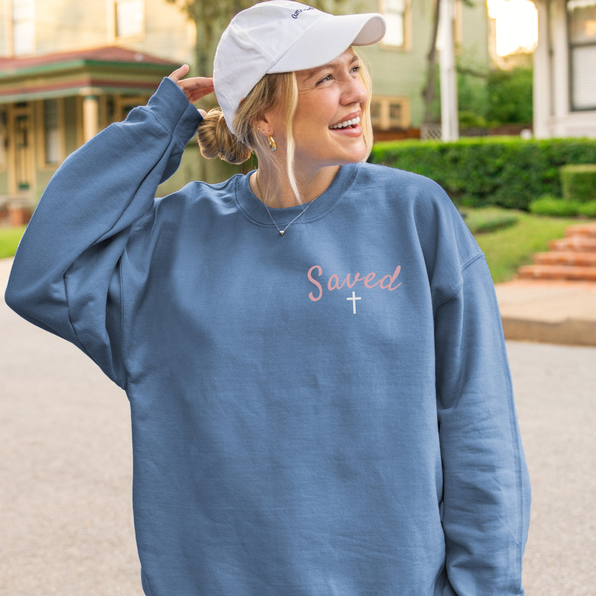 Woman wearing a blue sweatshirt with 'Saved' and a cross, outdoors.
