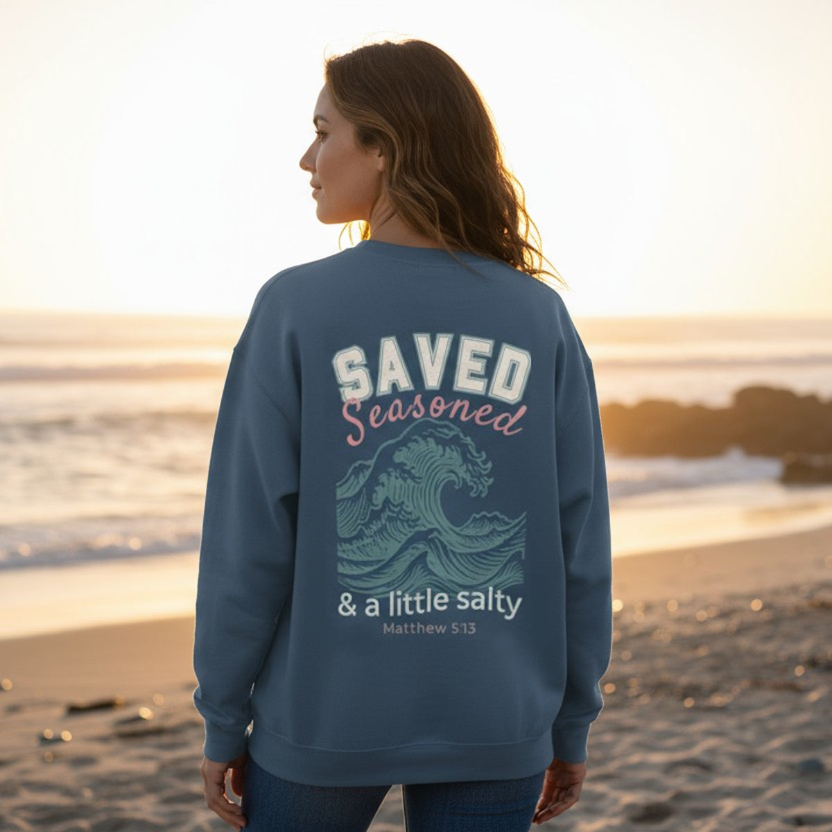 Person wearing a blue sweatshirt with a beach design and text on a beach at sunset.