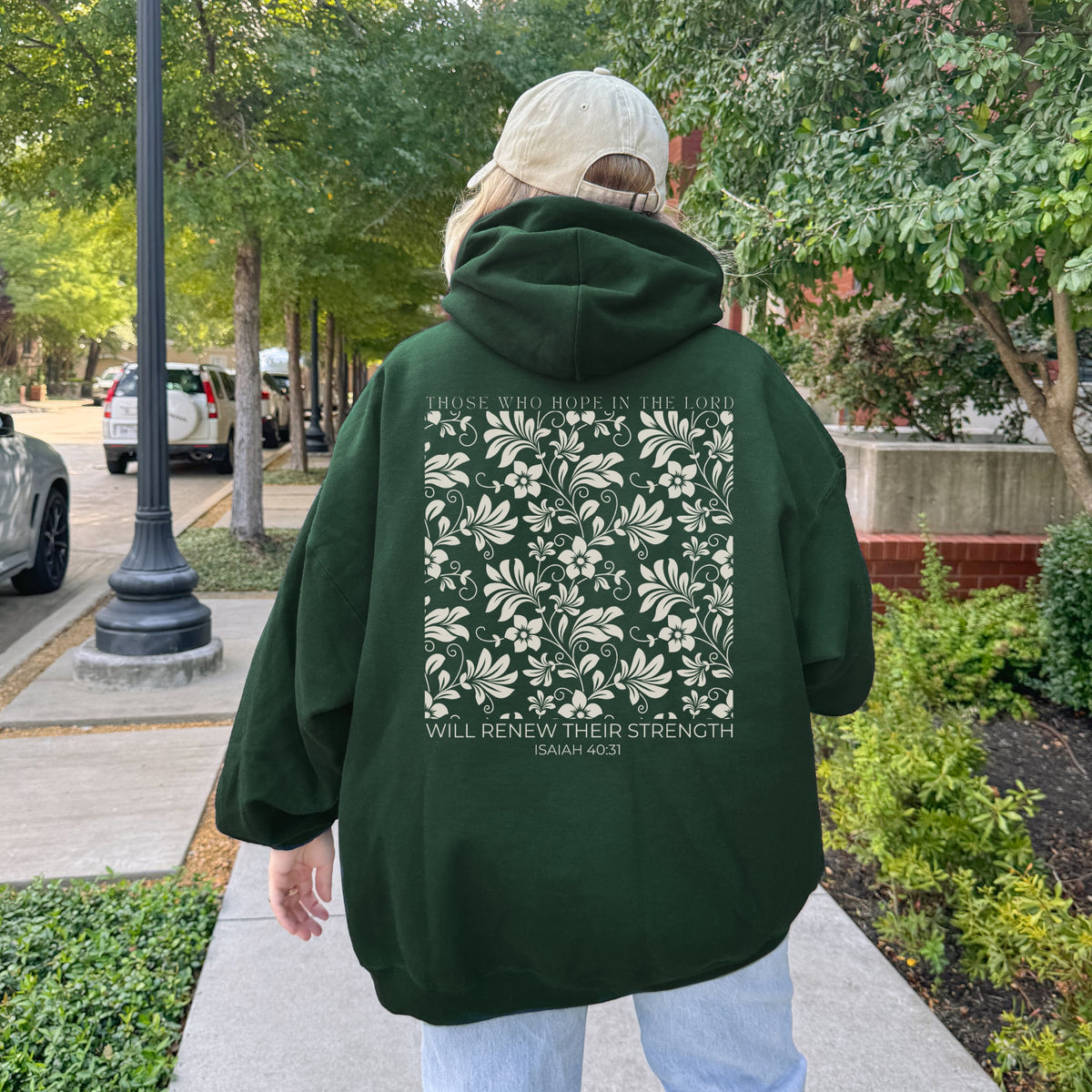 Person wearing a green hoodie with floral design and text on the back, walking outdoors.