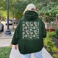 Person wearing a green hoodie with floral design and text on the back, walking outdoors.