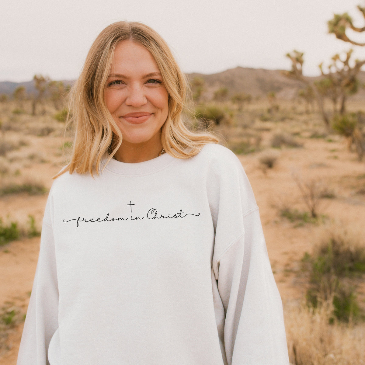 Person wearing a white sweatshirt with 'freedom in Christ' text in a desert setting