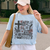 Woman wearing a light blue t-shirt with floral and cross design outdoors.
