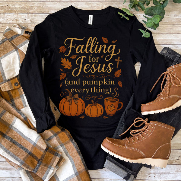 Black long-sleeve shirt with 'Falling for Jesus (and pumpkin everything)' text, surrounded by pumpkins and boots on a wooden surface.
