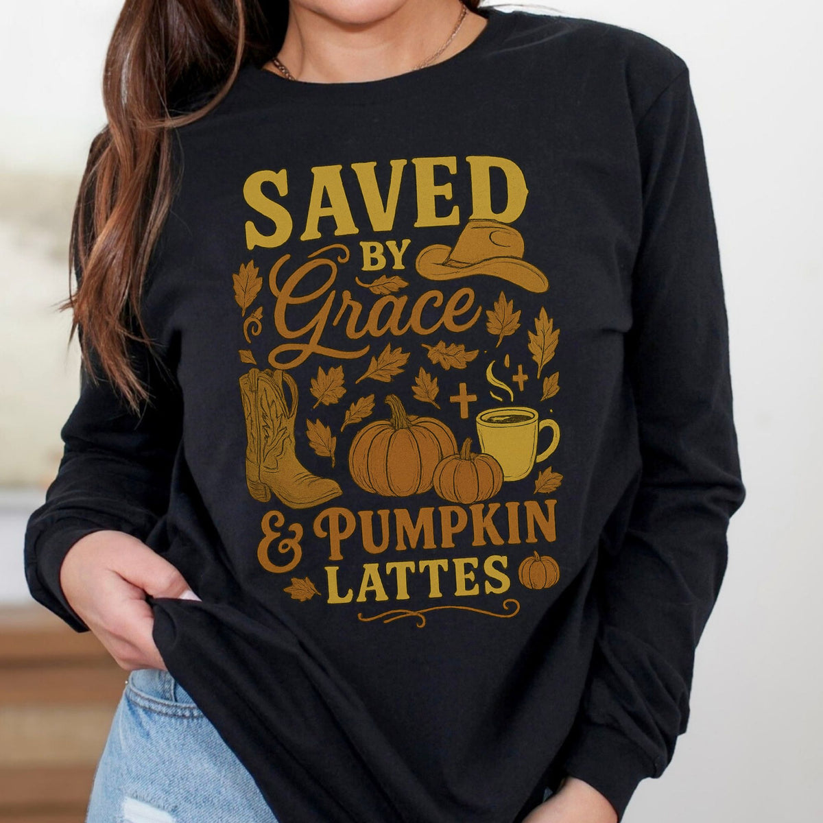 Black long-sleeve shirt with gold graphic and text 'Saved by Grace & Pumpkin Lattes' worn by a person.