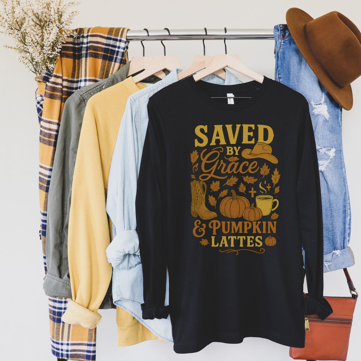 Black long sleeve t-shirt with autumn-themed design hanging on a rack with other clothing items.