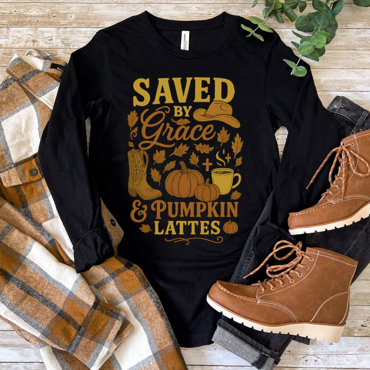 Black long-sleeve shirt with autumn-themed design and brown boots on a wooden surface.