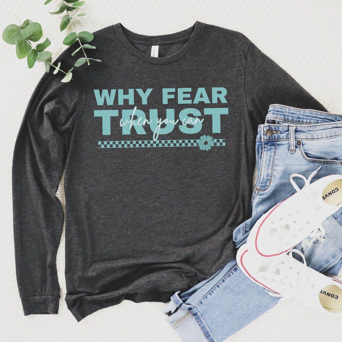 Dark gray long-sleeve shirt with motivational text, paired with jeans and sneakers on a light background.