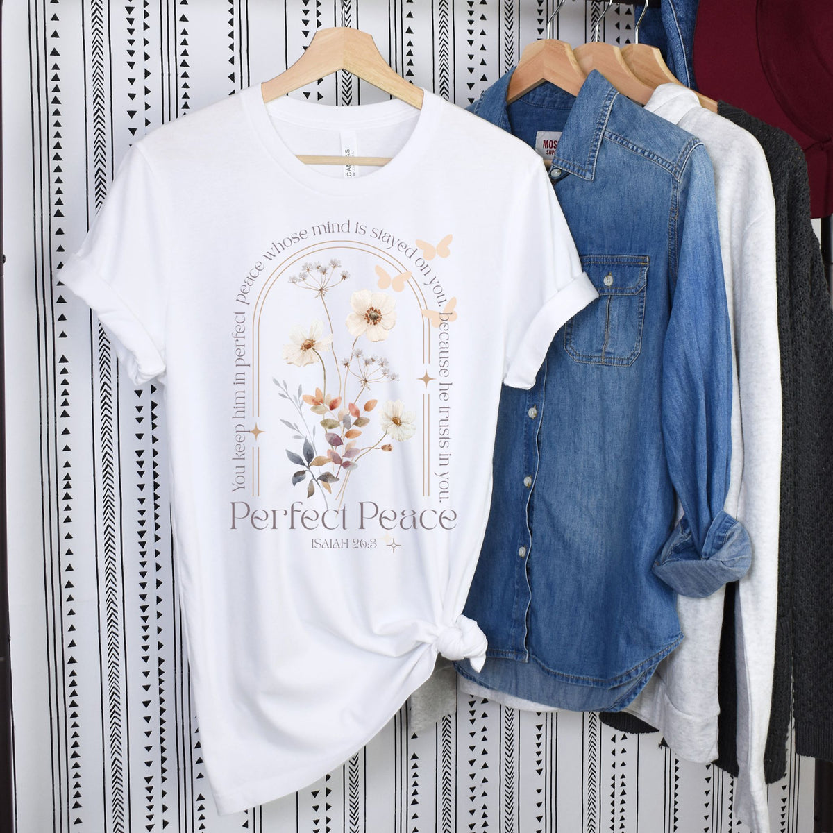 White t-shirt with floral design and text on a hanger against a patterned wall.