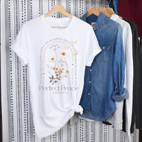 White t-shirt with floral design and text on a hanger against a patterned wall.