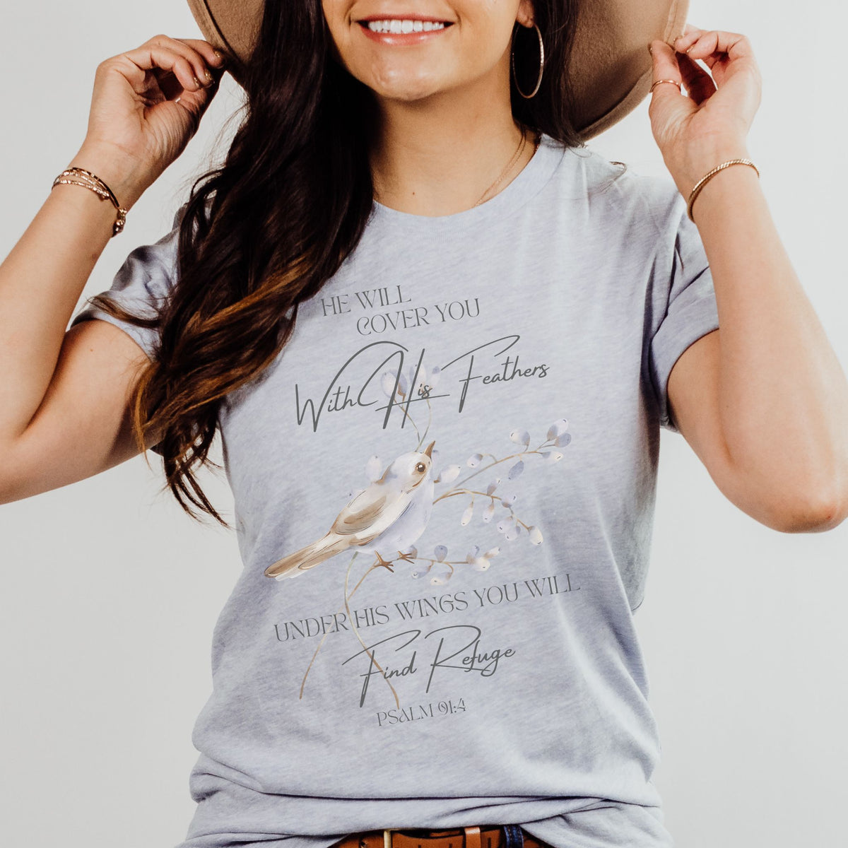 Woman wearing a t-shirt with a bird graphic and text, holding a hat.
