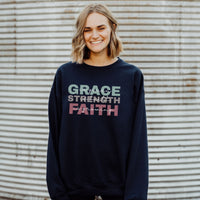 Person wearing a navy sweatshirt with 'GRACE STRENGTH FAITH' text against a corrugated metal background