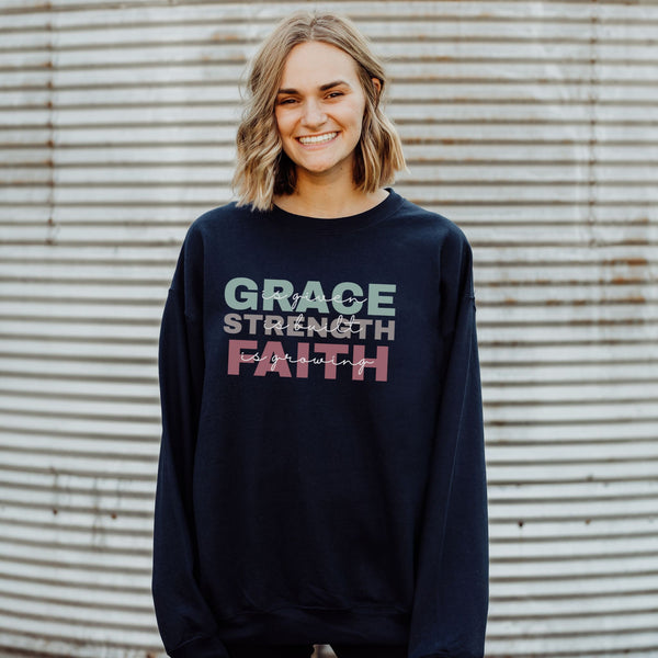 Person wearing a navy sweatshirt with 'GRACE STRENGTH FAITH' text against a corrugated metal background
