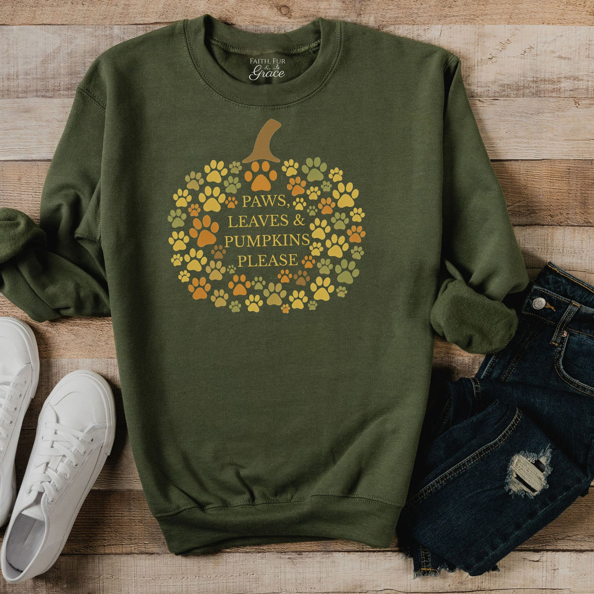 Green sweatshirt with pumpkin design and text on a wooden surface with shoes and jeans.