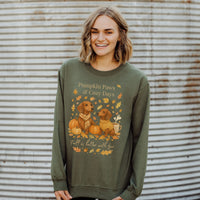 Woman wearing a green sweatshirt with 'Pumpkin Paws & Cozy Days' design against a corrugated metal background.