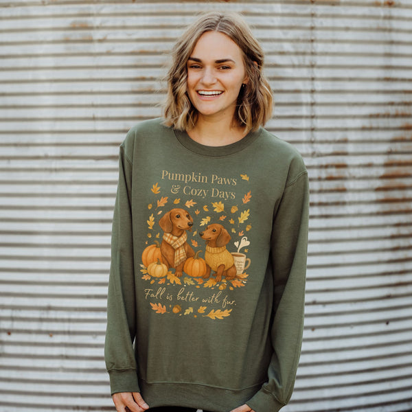 Woman wearing a green sweatshirt with 'Pumpkin Paws & Cozy Days' design against a corrugated metal background.