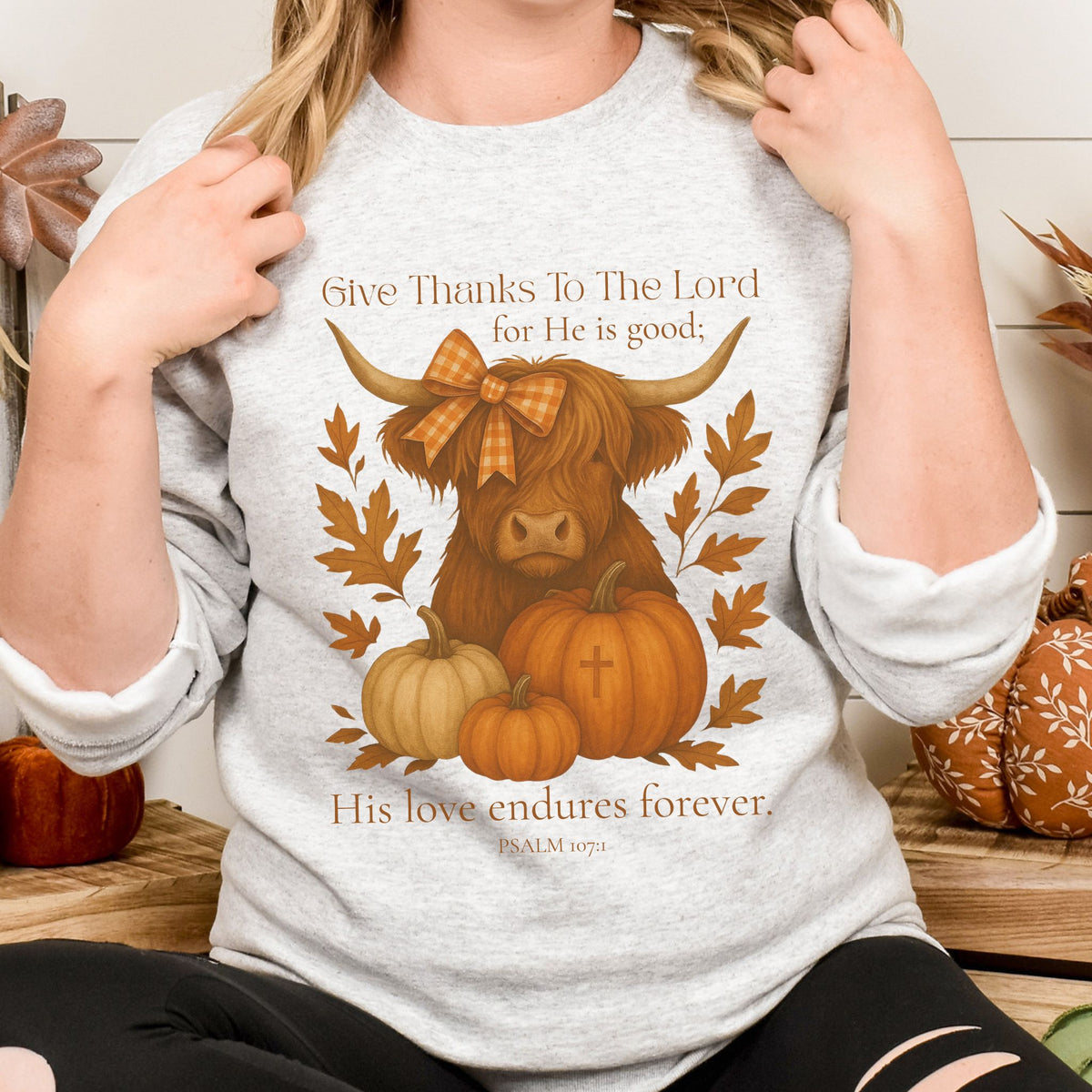 Person wearing a shirt with a cow, pumpkins, and fall leaves design with text.