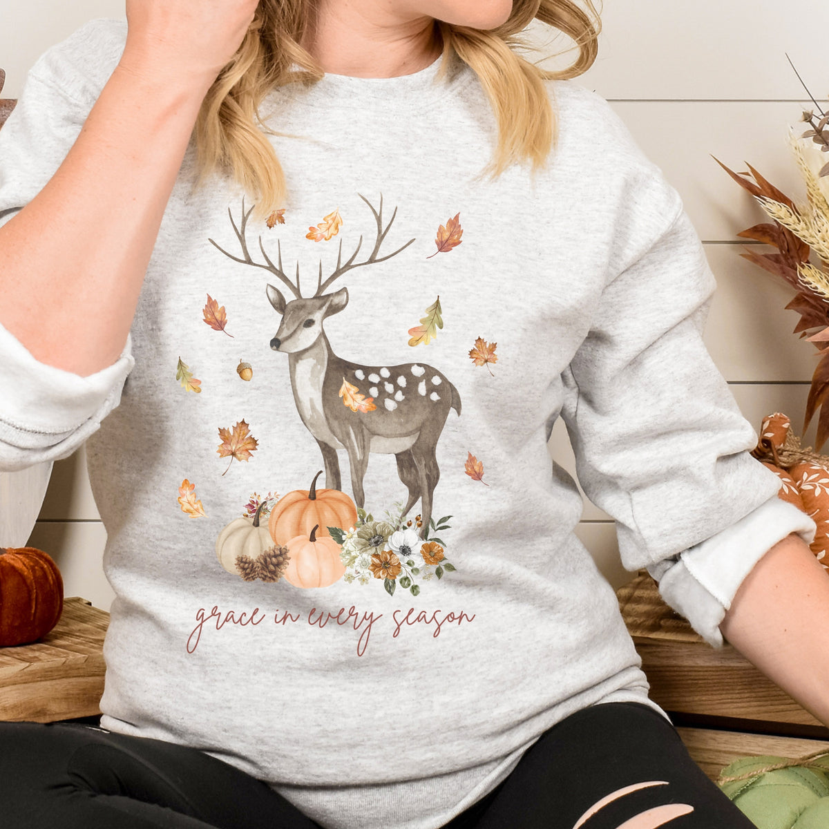 Person wearing a gray sweatshirt with a deer and autumn design.