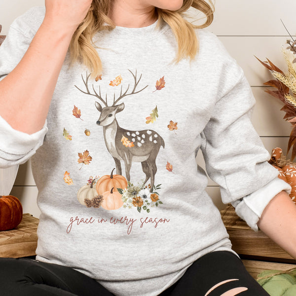 Person wearing a gray sweatshirt with a deer and autumn design.