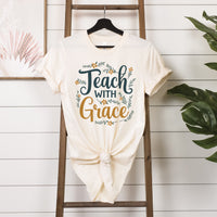 White t-shirt with 'Teach with Grace' text on a wooden ladder against a white wall.