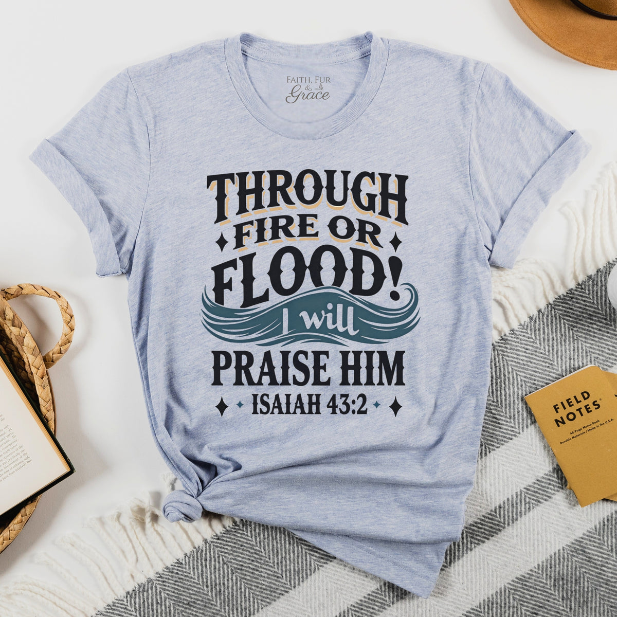 Light blue t-shirt with motivational quote on a white surface with books and a hat.