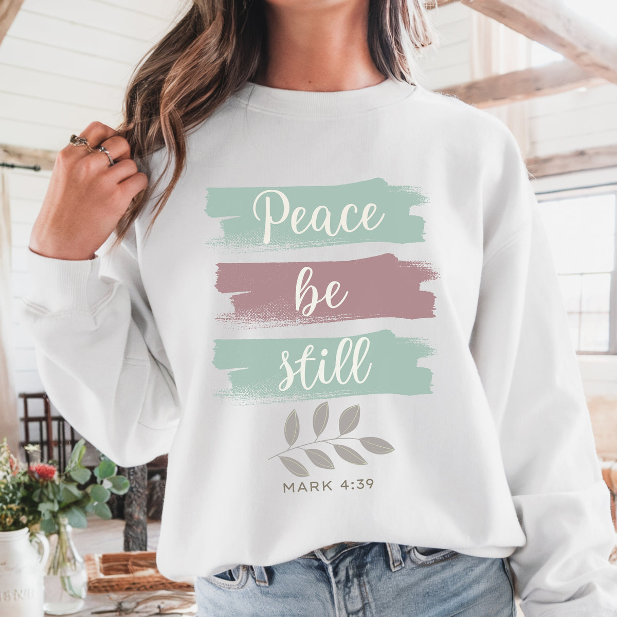 Person wearing a white sweatshirt with 'Peace be still' text and floral design.
