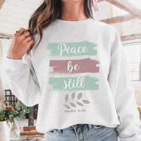 Person wearing a white sweatshirt with 'Peace be still' text and floral design.