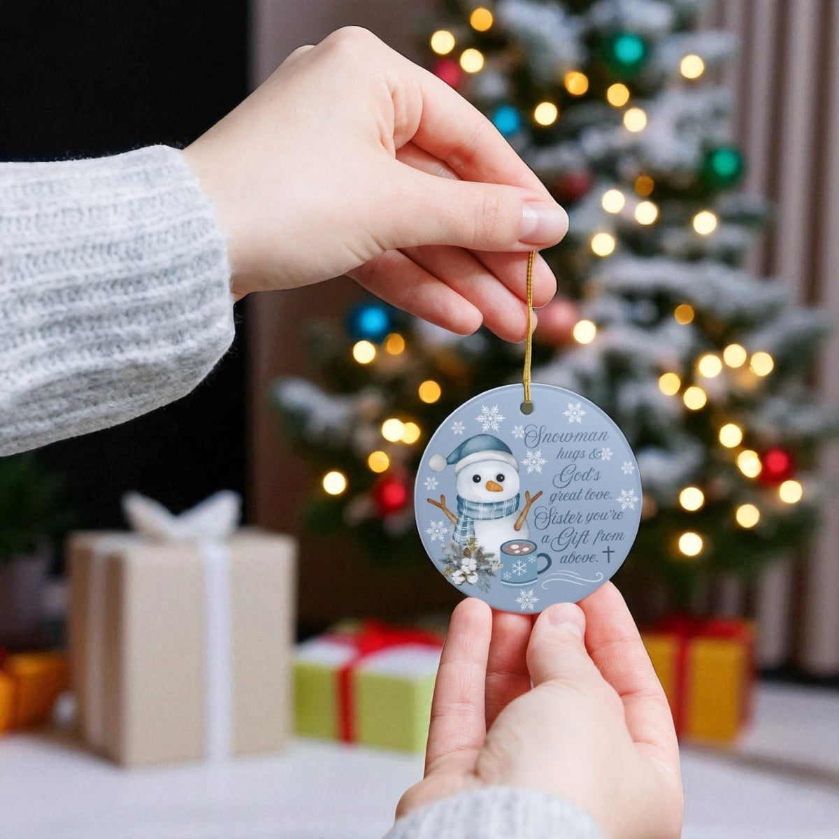 Person holding a Christmas ornament with a snowman design in front of a decorated Christmas tree.