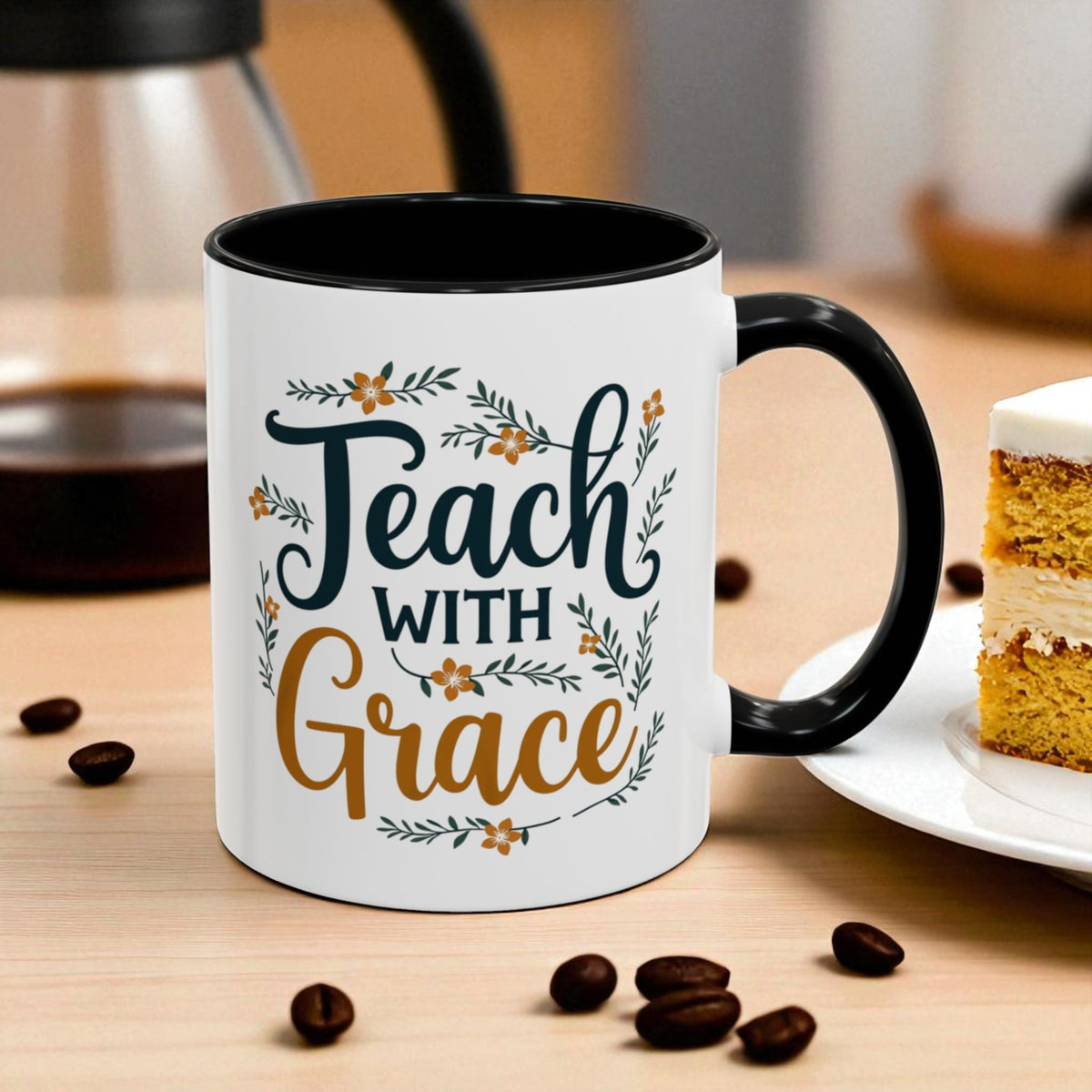 White mug with black interior and handle, featuring 'Teach with Grace' text on a wooden table with coffee beans and a slice of cake.