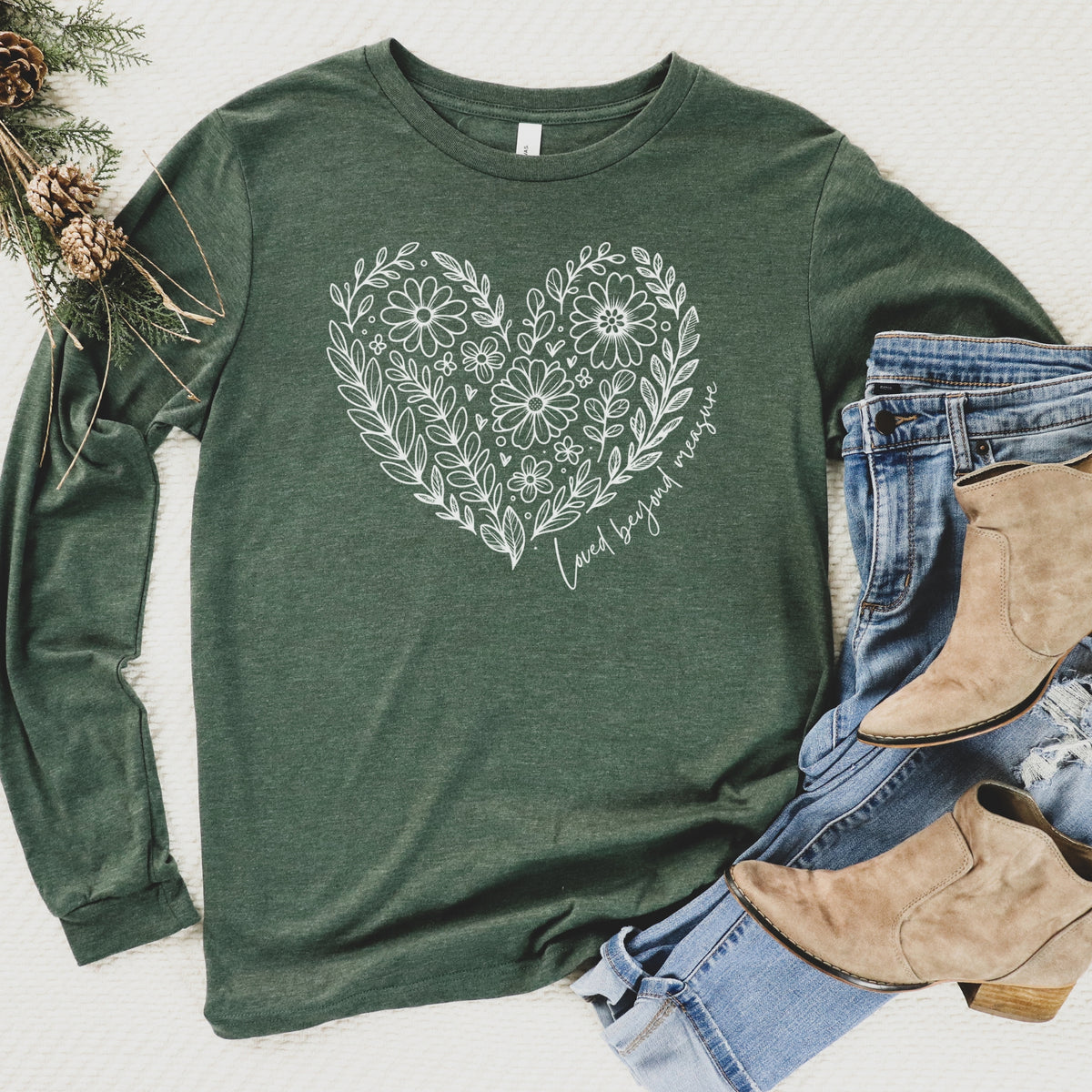 Green long-sleeve shirt with floral heart design, paired with jeans and boots on a light background.