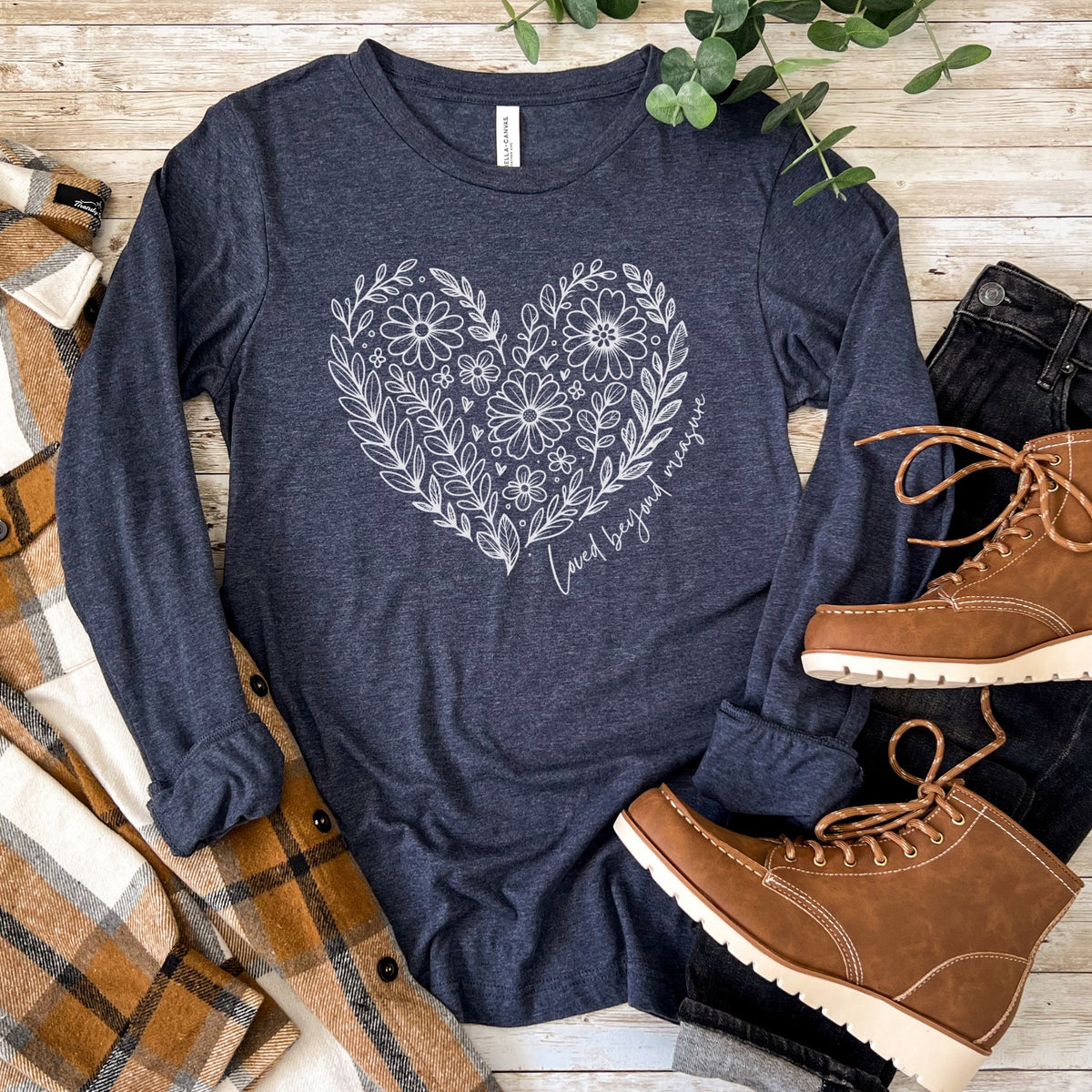 Navy blue long-sleeve shirt with floral heart design on a wooden surface with boots and plaid fabric.