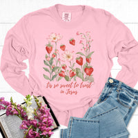 Pink long-sleeve shirt with floral design and text, paired with jeans and flowers on a white background