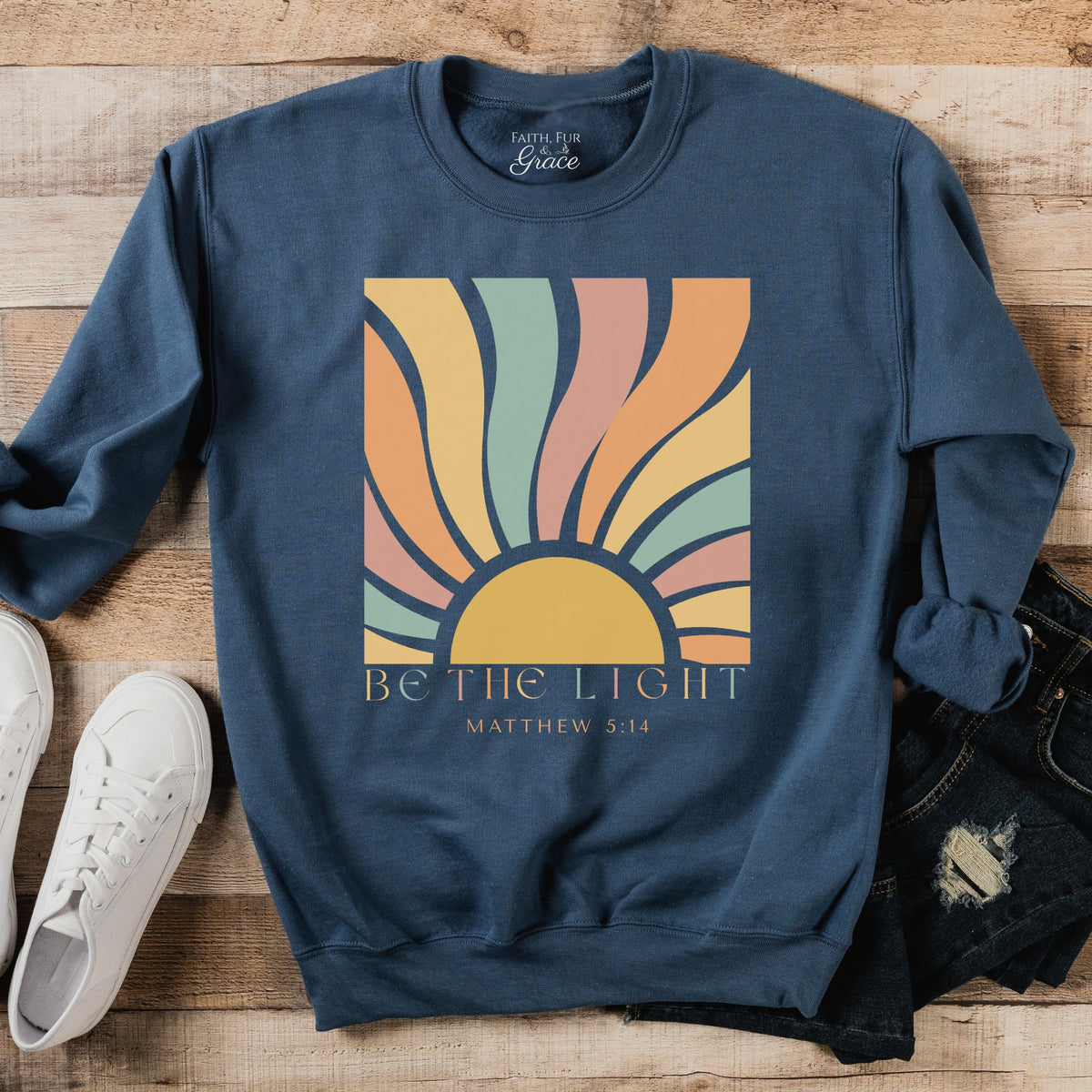 Blue sweatshirt with colorful sun design and text on a wooden surface