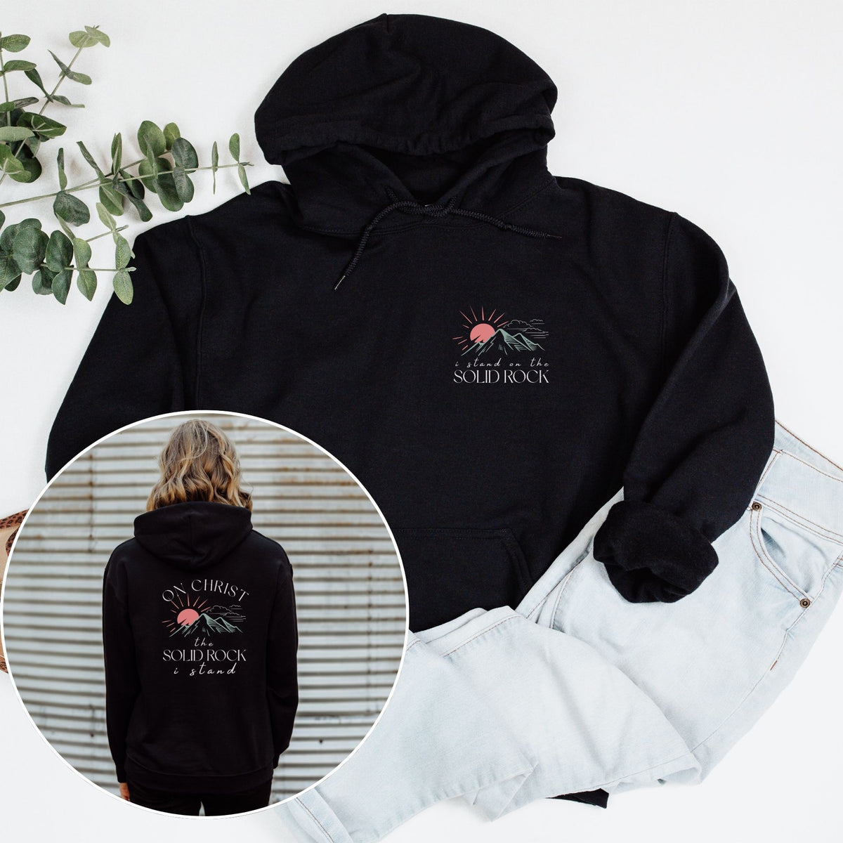 Black hoodie with a design on the front and back, displayed with jeans and a plant.
