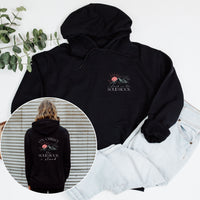 Black hoodie with a design on the front and back, displayed with jeans and a plant.