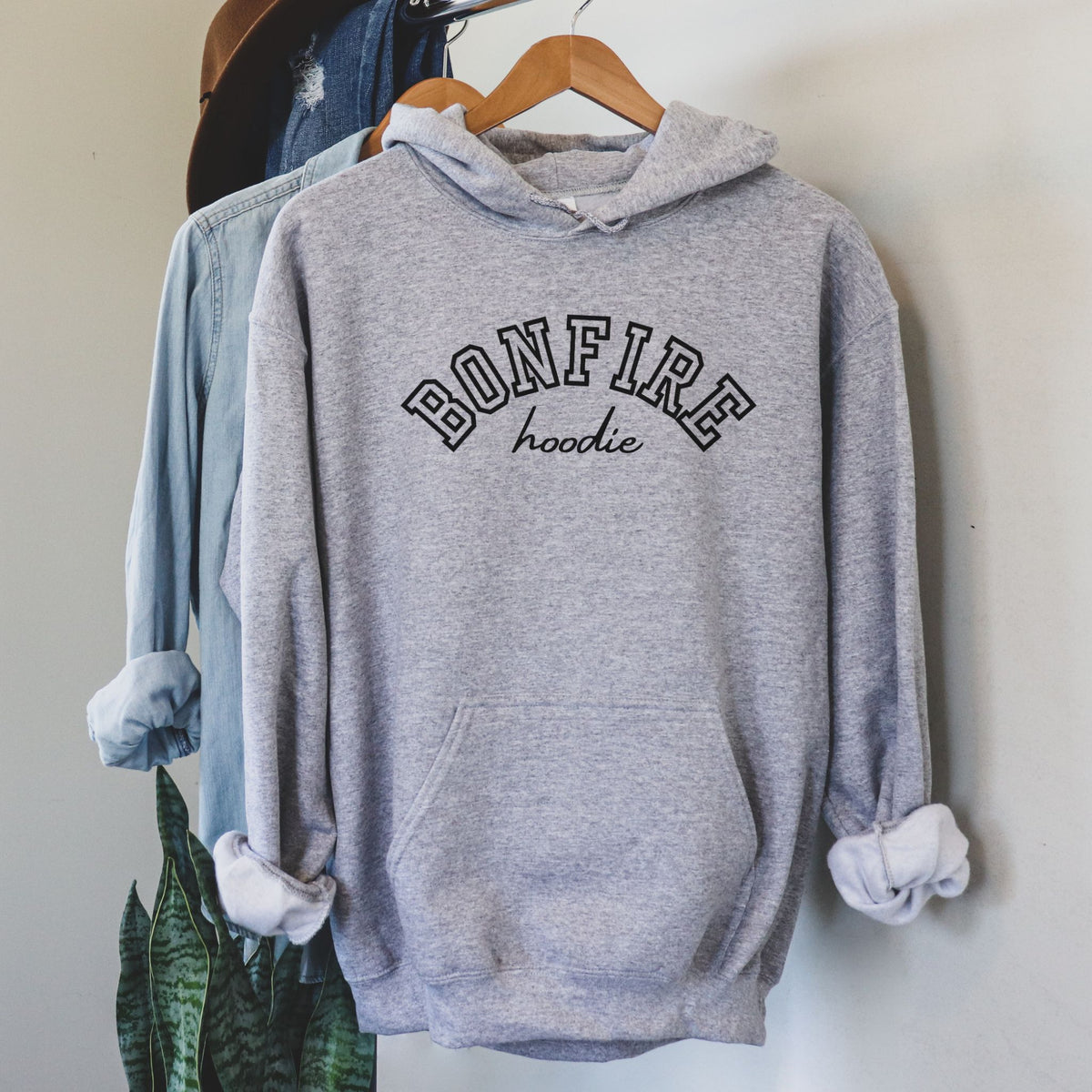 Gray hoodie with 'BONFIRE hoodie' text on a hanger against a neutral wall.