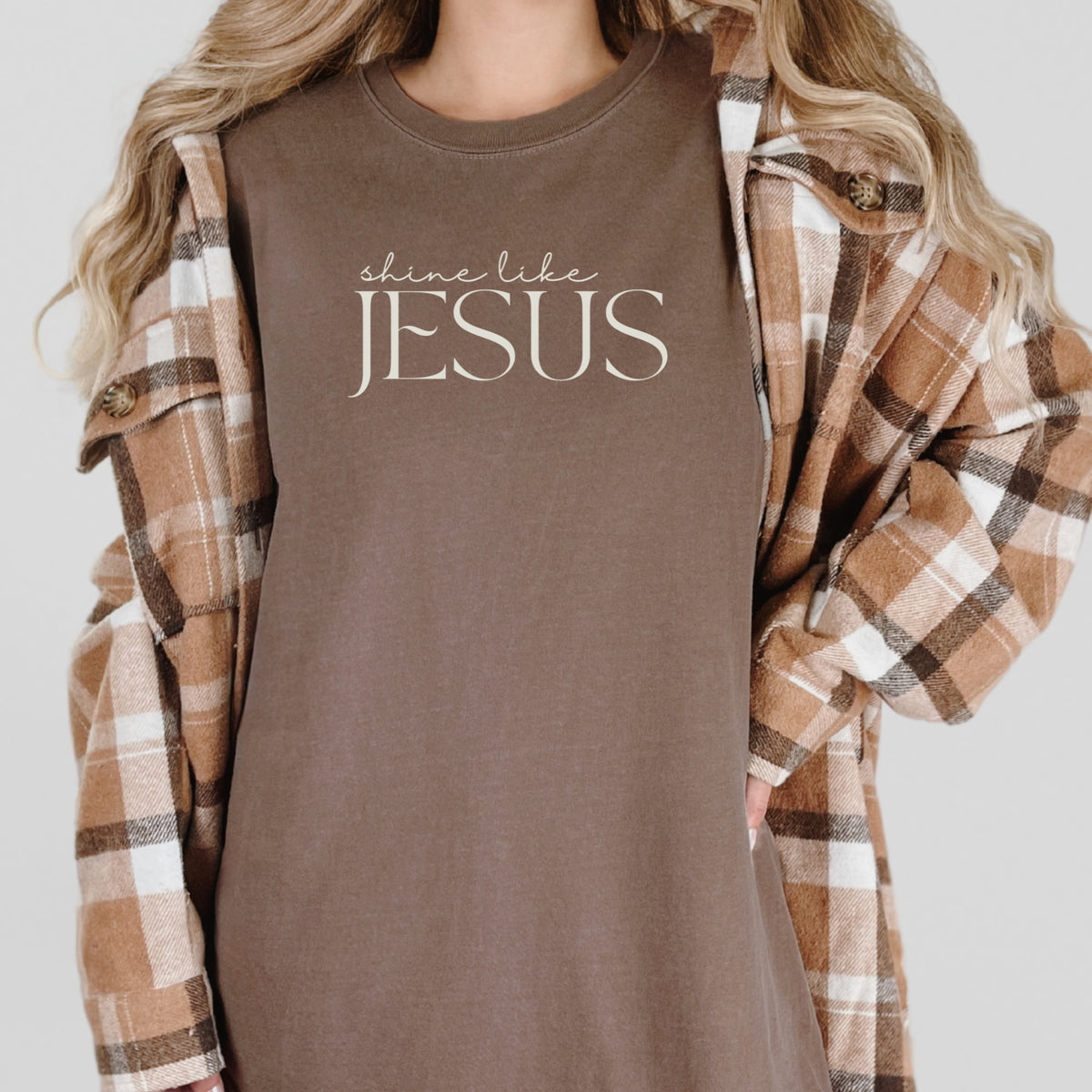 Person wearing a brown shirt with 'shine like JESUS' text, paired with a plaid jacket.