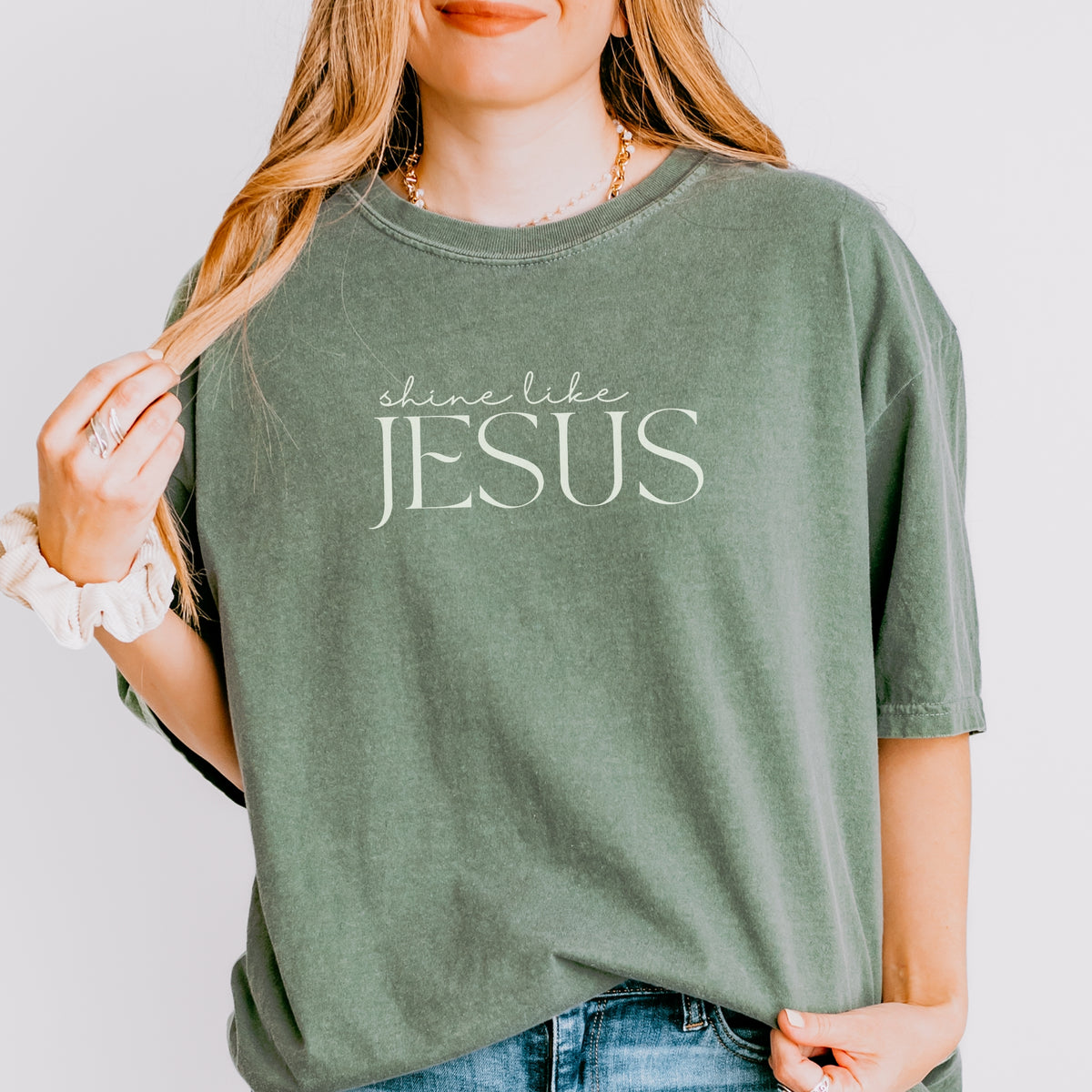 Person wearing a green t-shirt with 'shine like JESUS' text on a plain background