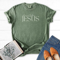 Green t-shirt with 'shine like Jesus' text on a white wooden surface with books and shoes.