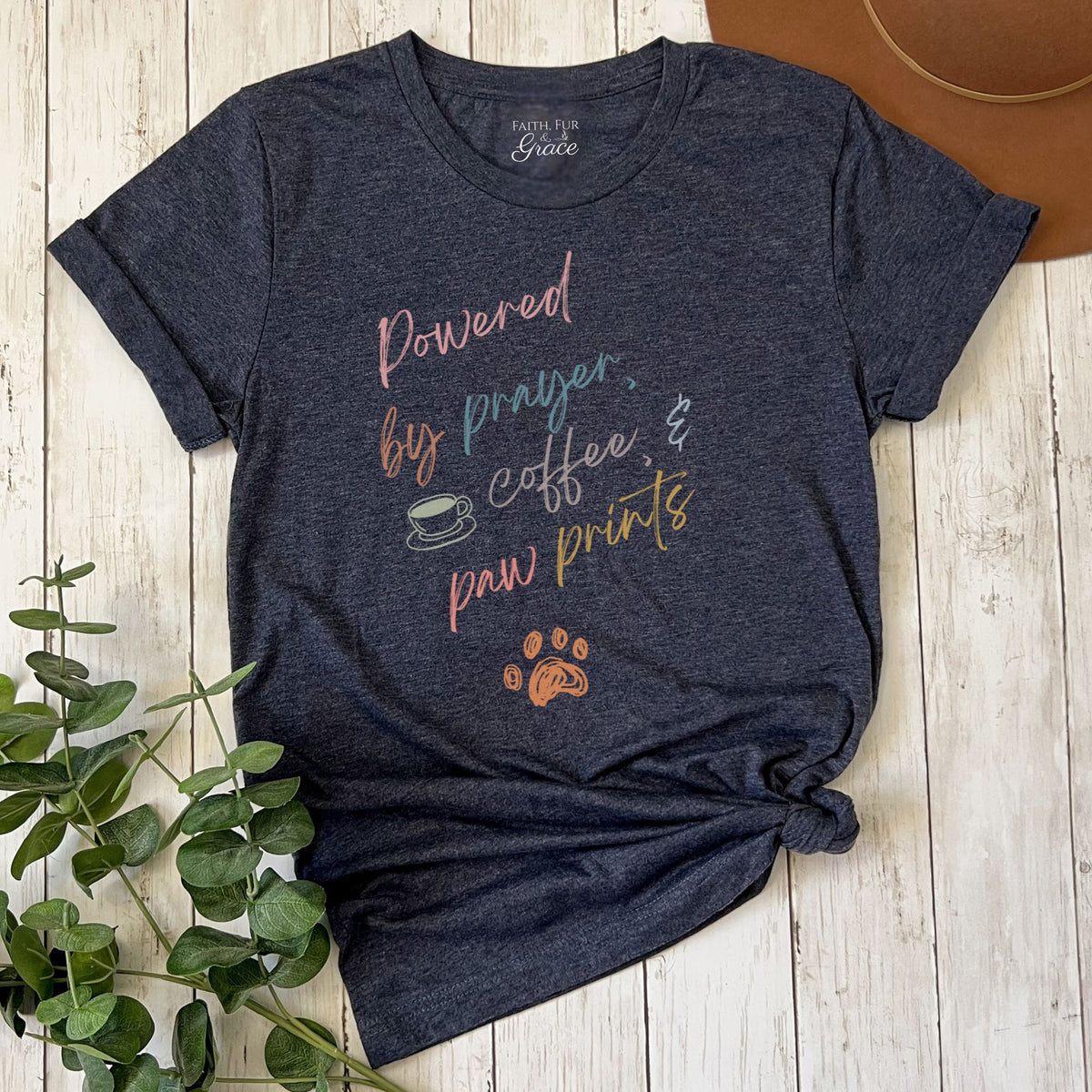 Navy blue t-shirt with motivational text and graphics on a wooden surface with a plant.