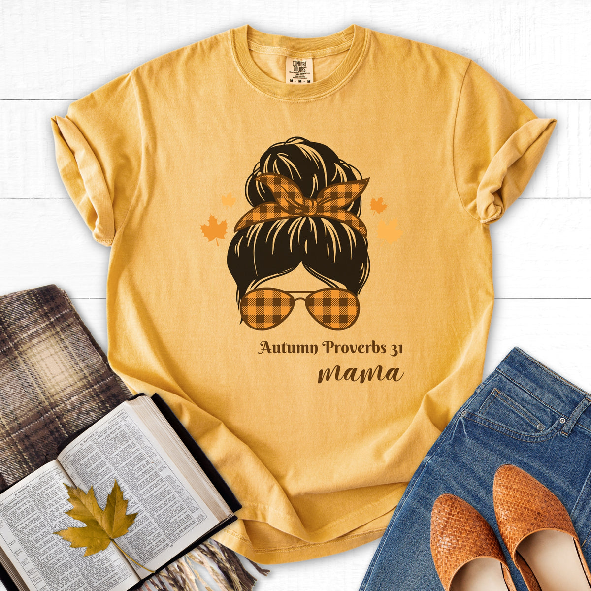 Yellow t-shirt with a graphic design of a woman's head with sunglasses and text, placed on a white surface with books and shoes.
