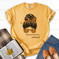 Yellow t-shirt with a graphic design of a woman's head with sunglasses and text, placed on a white surface with books and shoes.