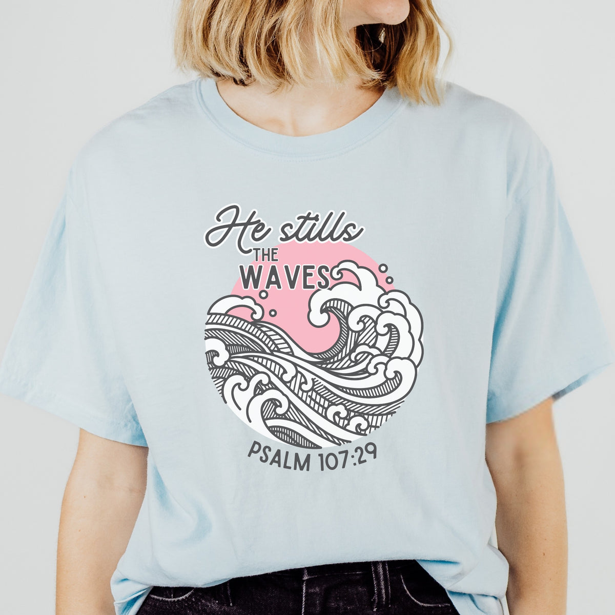 Light blue t-shirt with wave design and text worn by a person on a plain background