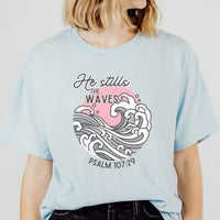 Light blue t-shirt with wave design and text worn by a person on a plain background