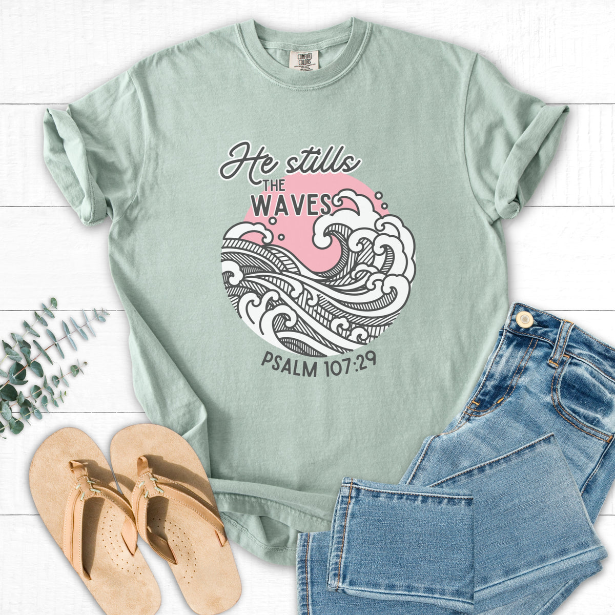 Green t-shirt with wave design and text, paired with jeans and sandals on a white background