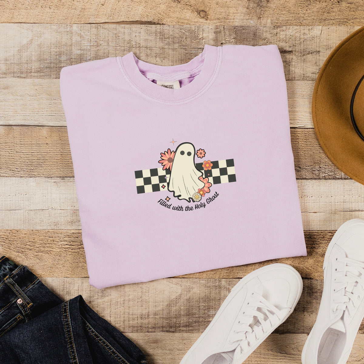 Folded light purple sweatshirt with a ghost design on a wooden surface